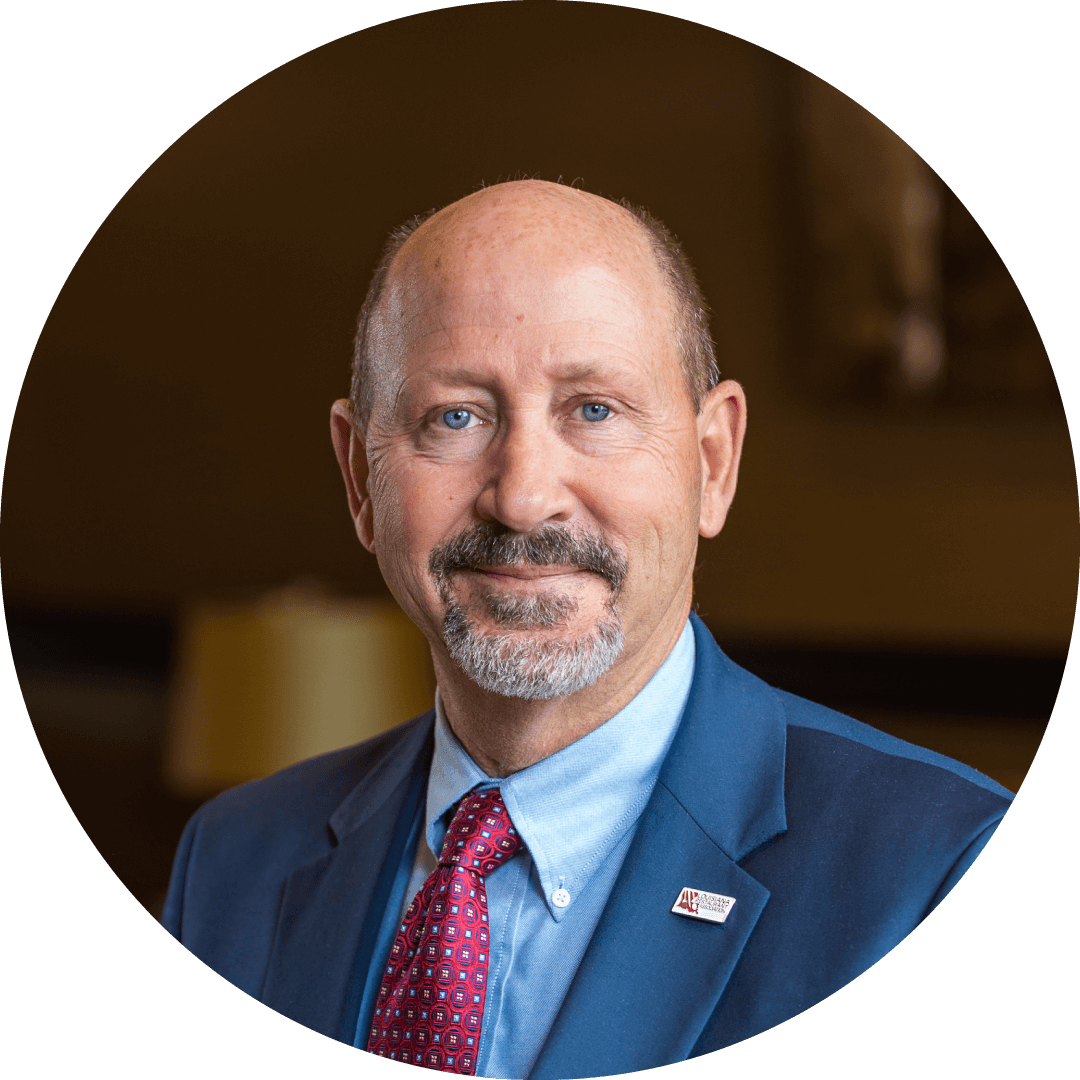 Older white male, blue eyes, bald, mustache, goatee, red tie, light blue shirt