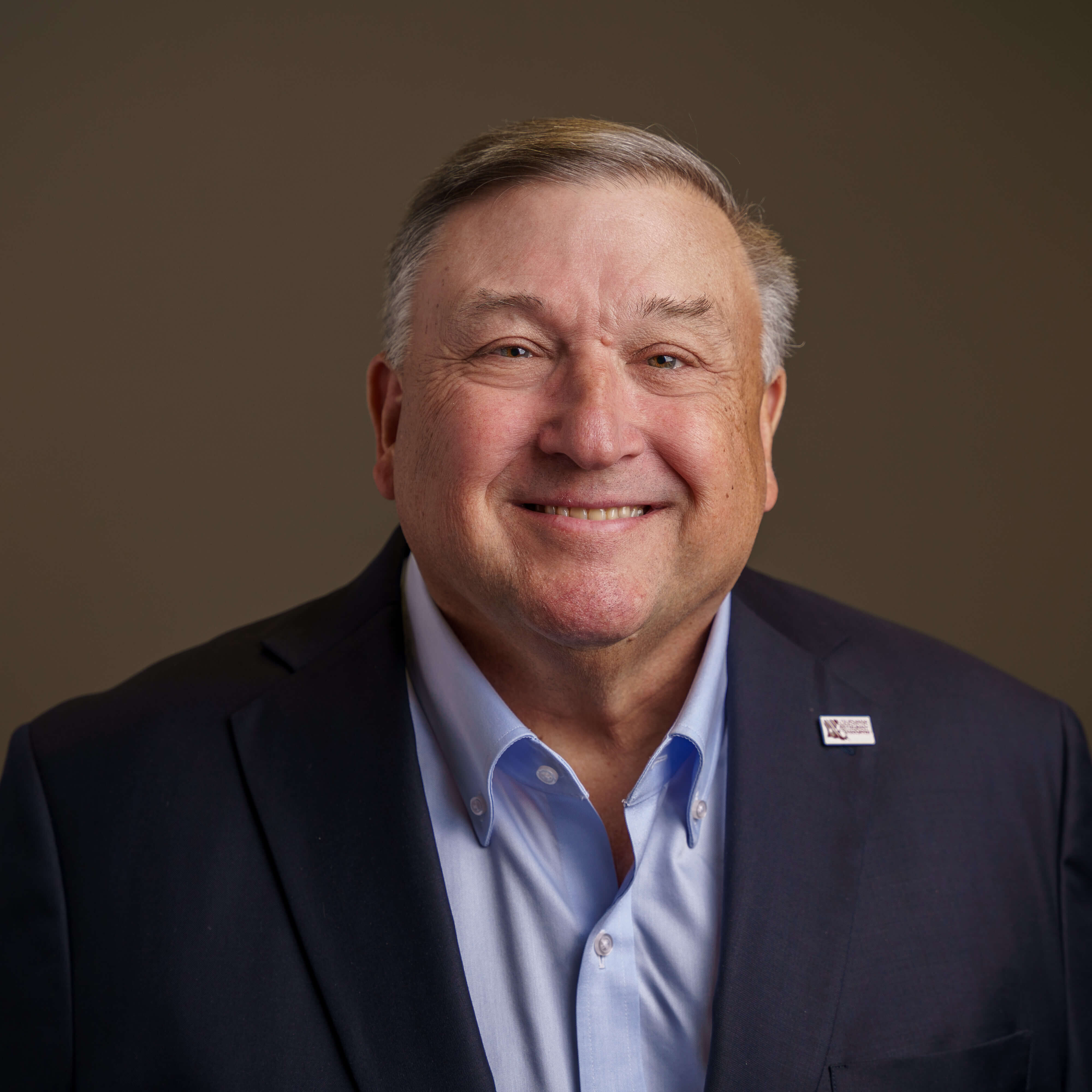 White Male, happily smiling, wearing navy blue suit jacket and light blue shirt